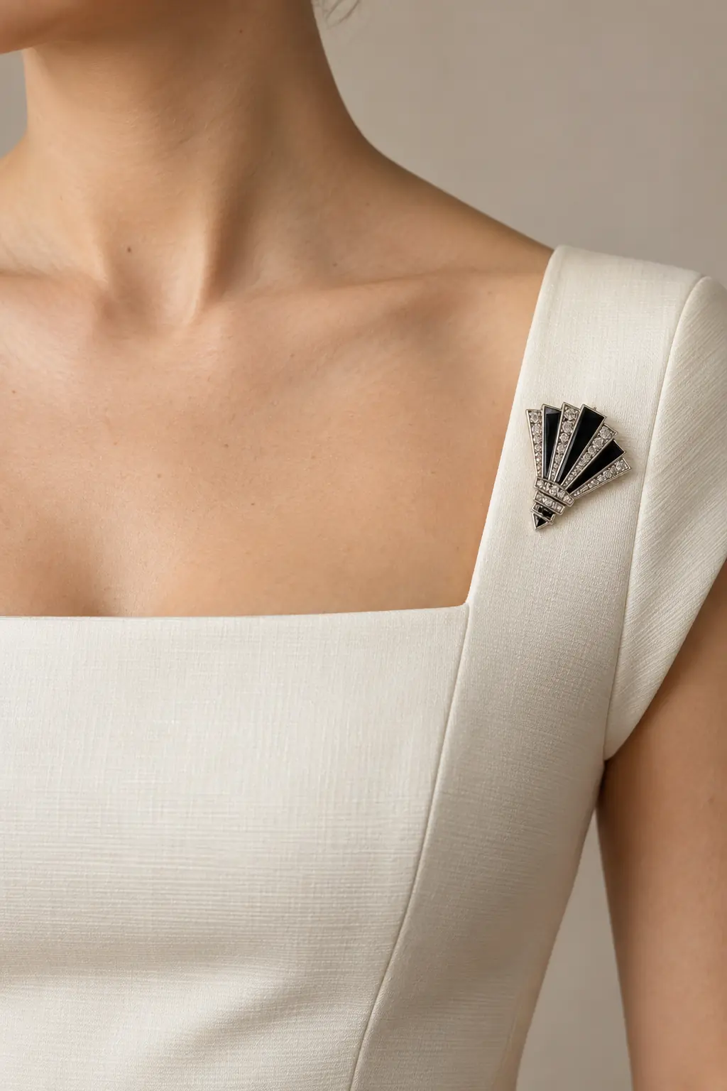 Silver and black enamel Art Deco fan brooch at the outer corner of an ivory square-neck dress