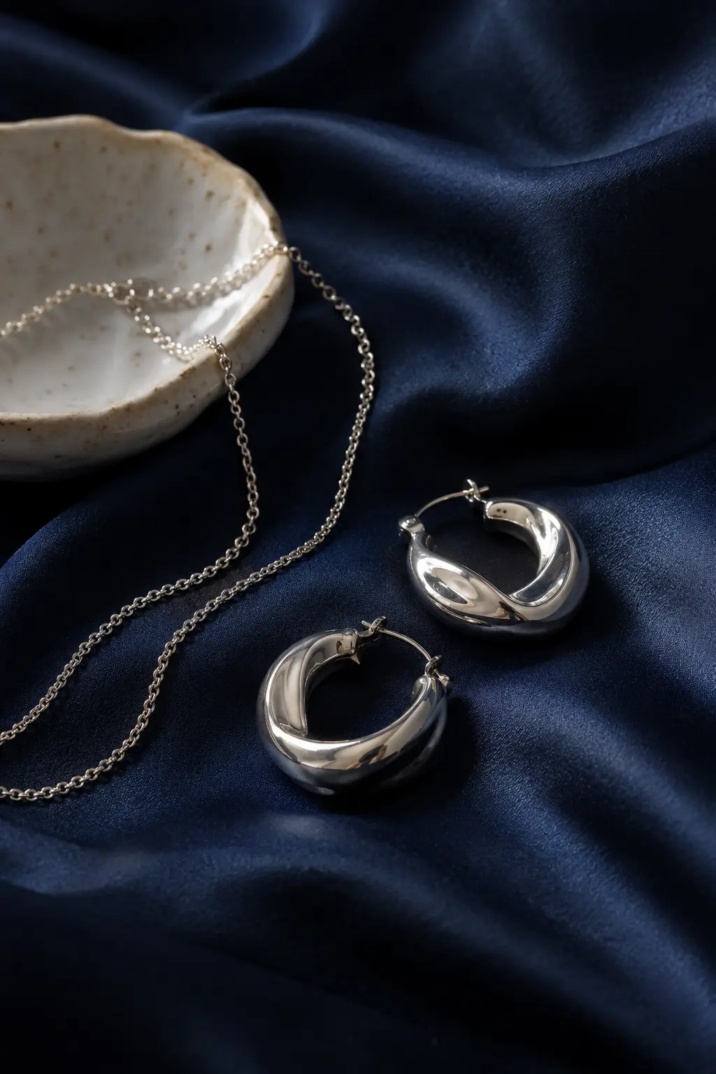 Sculptural silver hoops and a fine chain on midnight blue satin