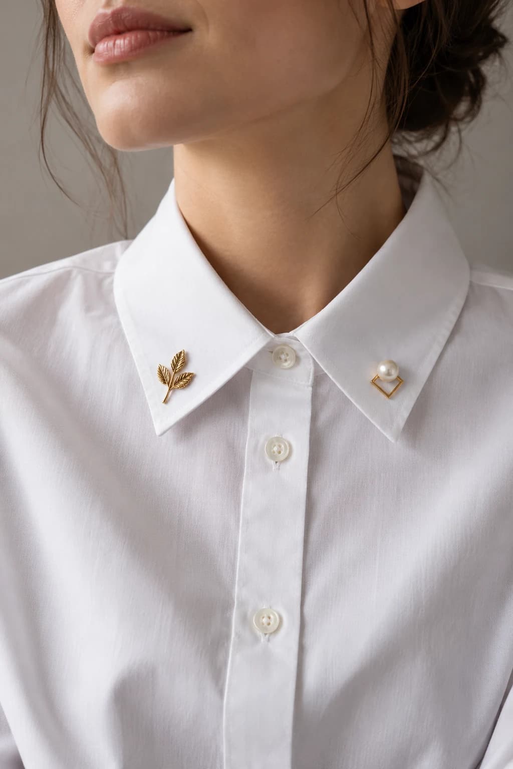 Small gold leaf and pearl geometric brooches pinned to the points of a white shirt collar