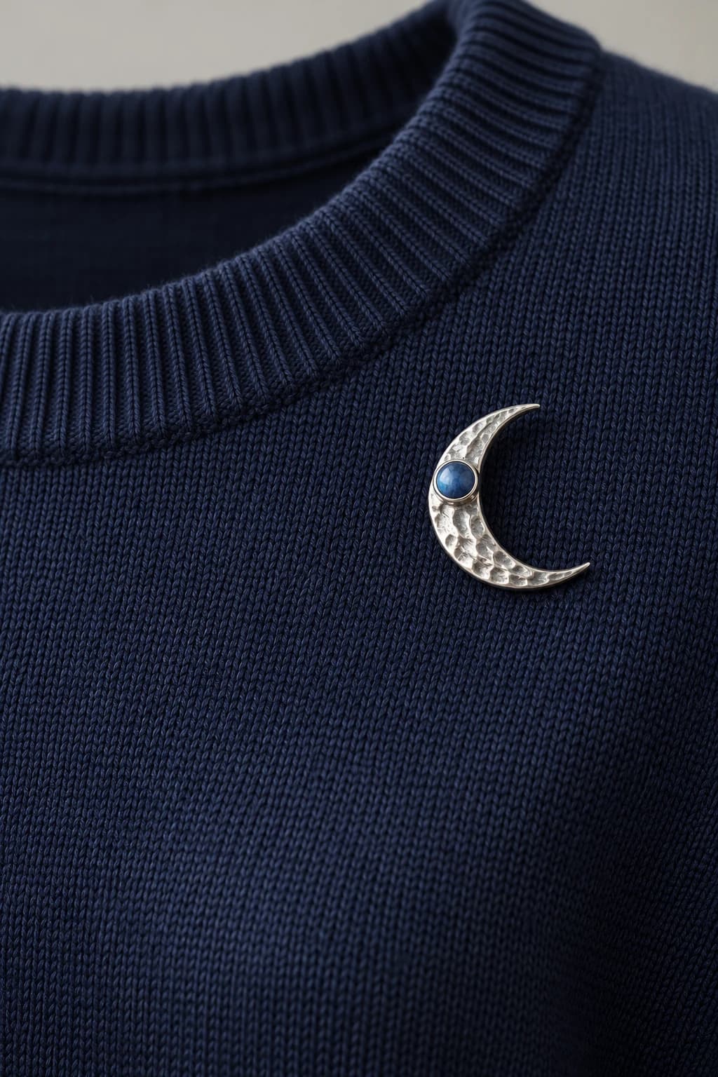 Silver crescent brooch with a blue stone below the neckline of a navy knitted sweater
